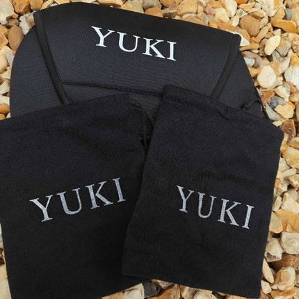 Three black fabric pouches or small bags with the name 'YUKI' embroidered in white on the front, arranged on a bed of small tan and gray pebbles.